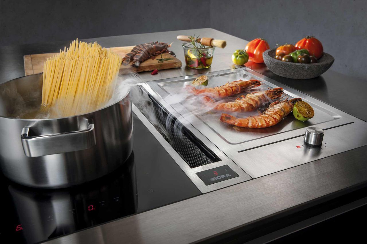 Mujer cocinando en la cocina en una placa de inducción con extractor de  olores